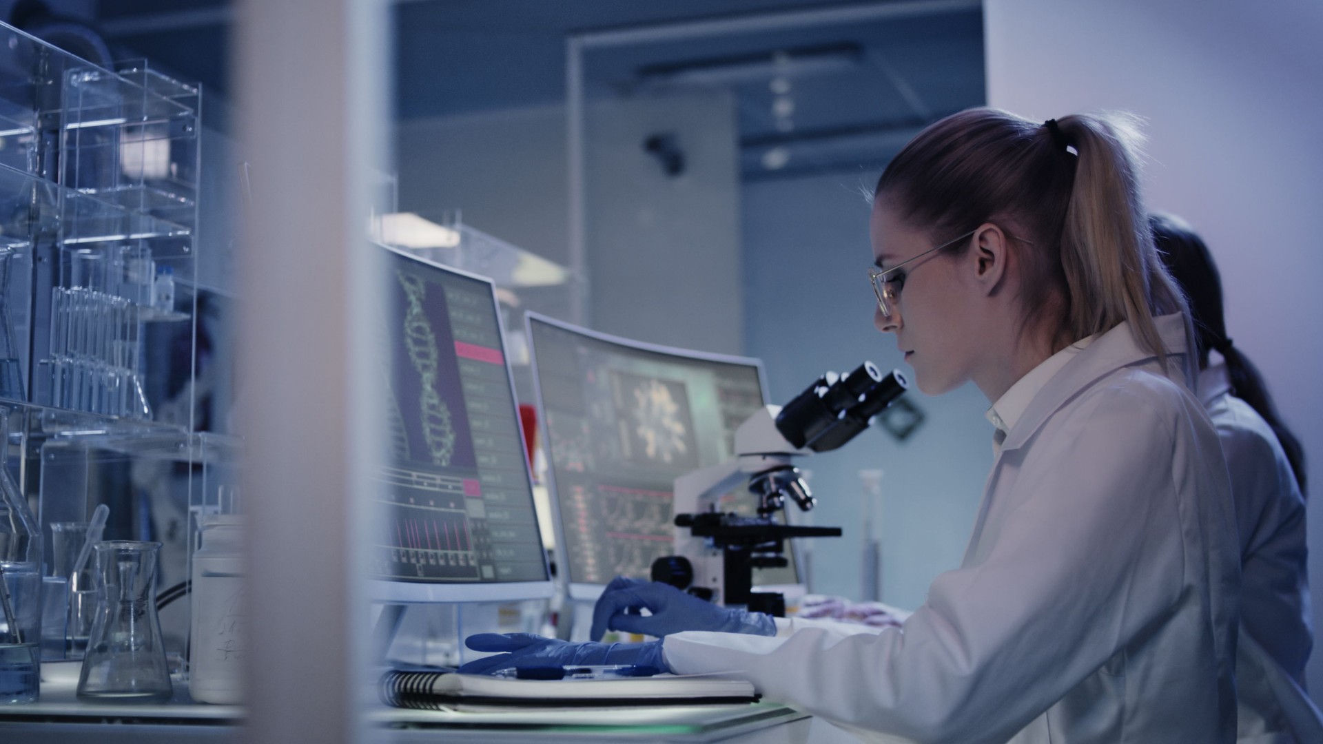 Female research team studying DNA mutations. Computer screens with DNA helix in foreground